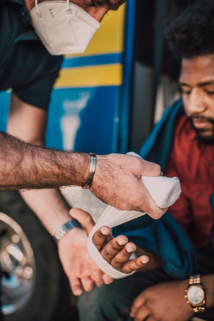 A healthcare worker providing first aid bandaging to an injured man's hand.